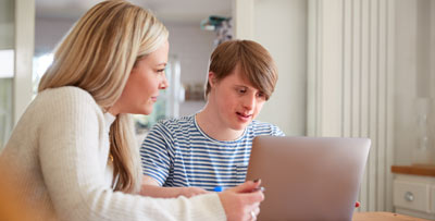 A carer helping a patient with downs syndrome use a laptop